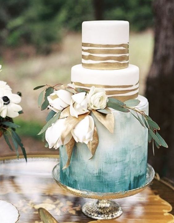 a fine art wedding cake with watercolor blues and gold stripes plues white blooms and gilded leaves