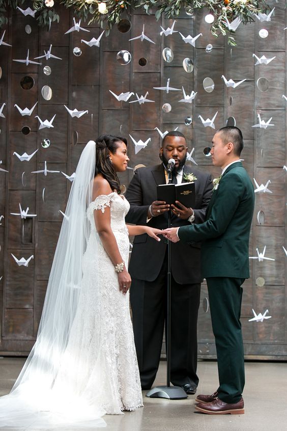 a wedding backdrop made of paper cranes and couple's photos plus greenery on top