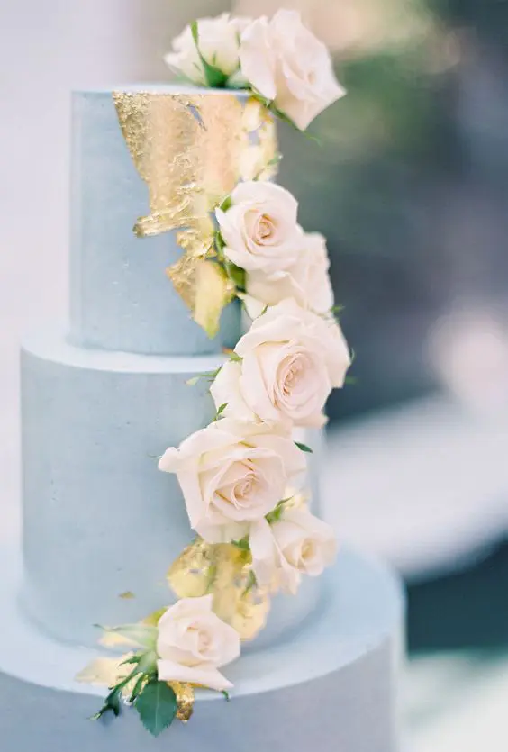 a chic dusty blue wedding cake with gold leaf decor and cascading blush roses