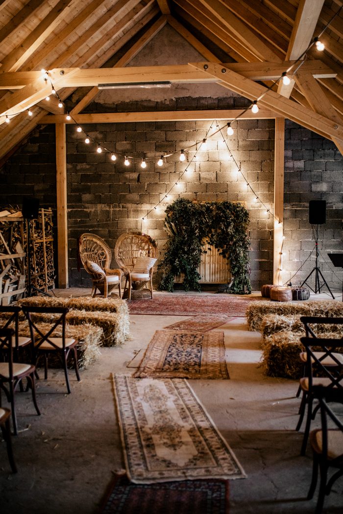 The wedding ceremony space was done with hay, boho rugs, boho woven chairs and a lush greenery and feather backdrop