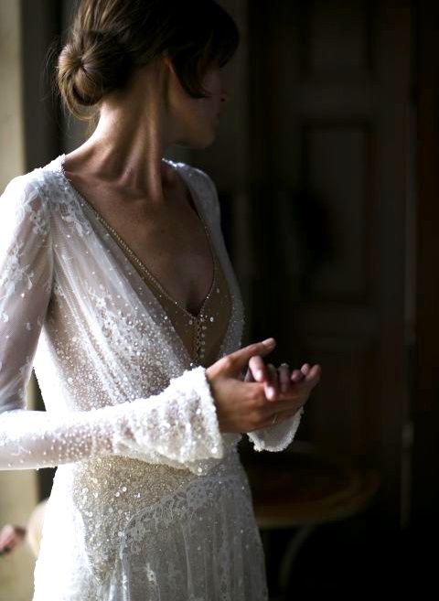a heavily embellished lace applique wedding dress with bell sleeves and a nude buttoned bodice
