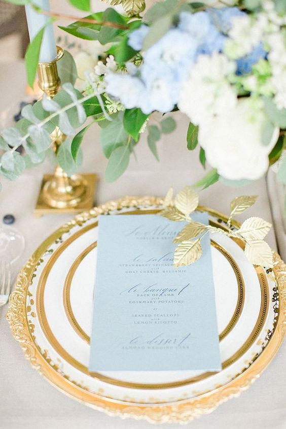 an exquisite wedding tablescape with blue florals, a gold edge plates and chargers plus gold candle holders