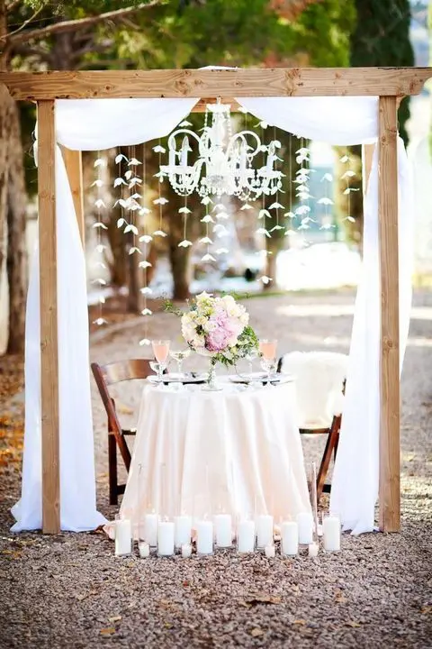 a sweetheart table placed under an arch with a glam chandelier and paper cranes