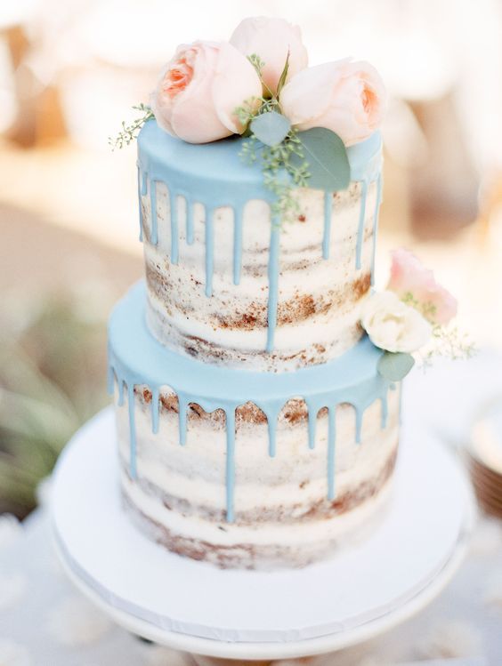 a semi-naked wedding cake with light blue dripping and blush blooms on top