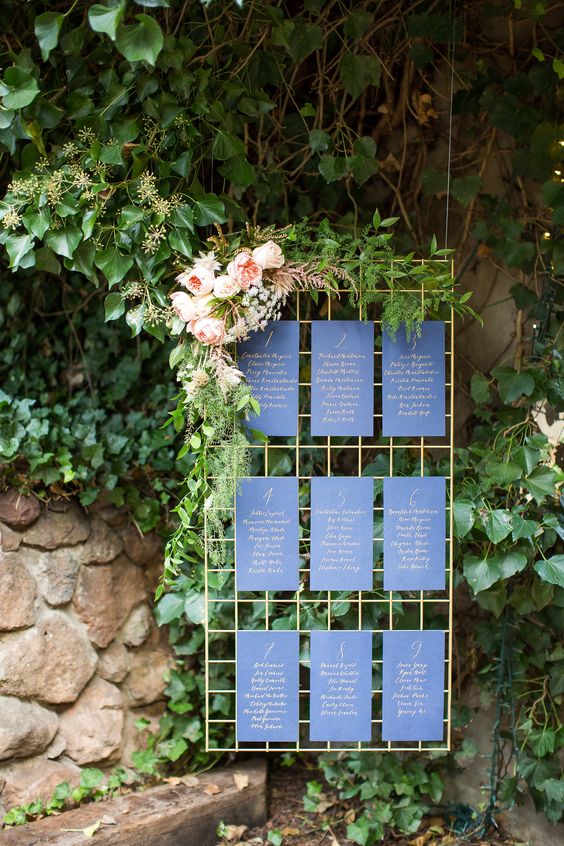 a gilded metal grid with navy and gold seating chart sheets and fresh greenery and flowers