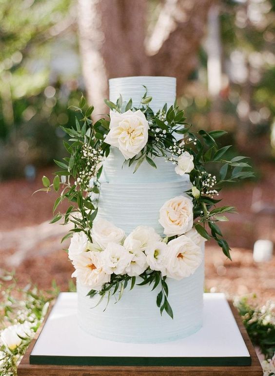 a romantic light blue wedding cake with greenery and neutral blooms