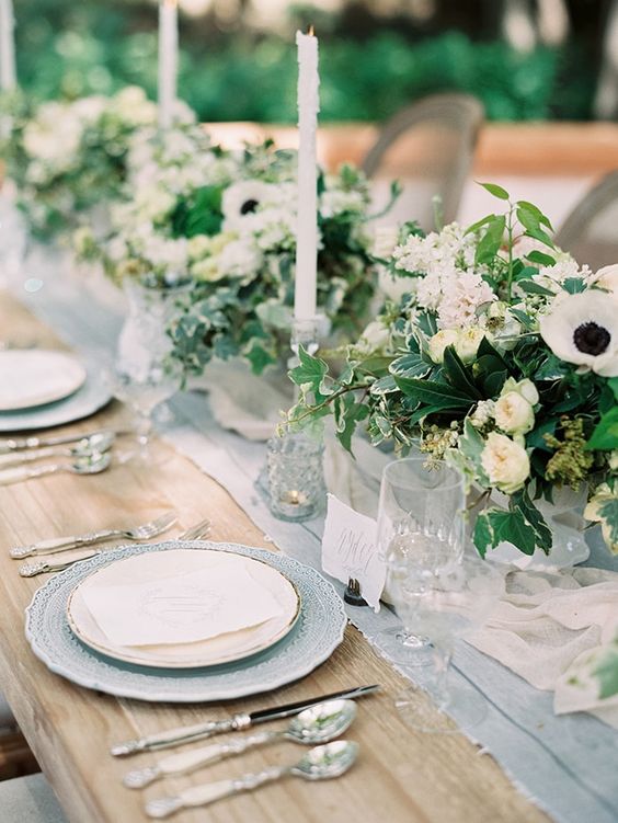 a stunning wedding tablescape with a blue runner and chargers, white floral centerpieces and plates