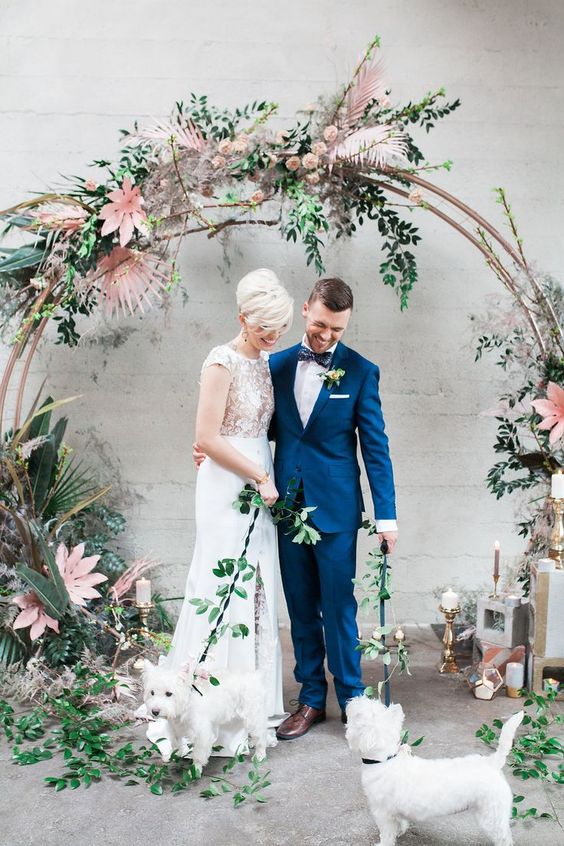 a large tropical-inspired wedding arch covered with bold leaves and blooms and candles around
