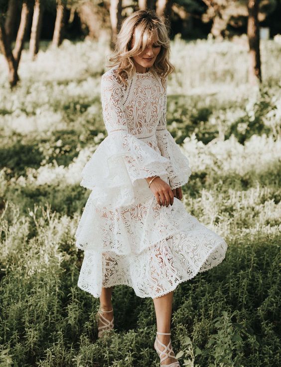 a lace wedding dress with a high neckline, bell sleeves and a layered skirt to stand out