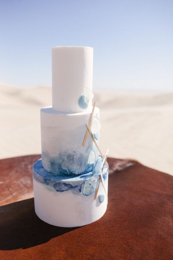 a watercolor wedding cake in the shades of blue, with sticks attached for a coastal wedding