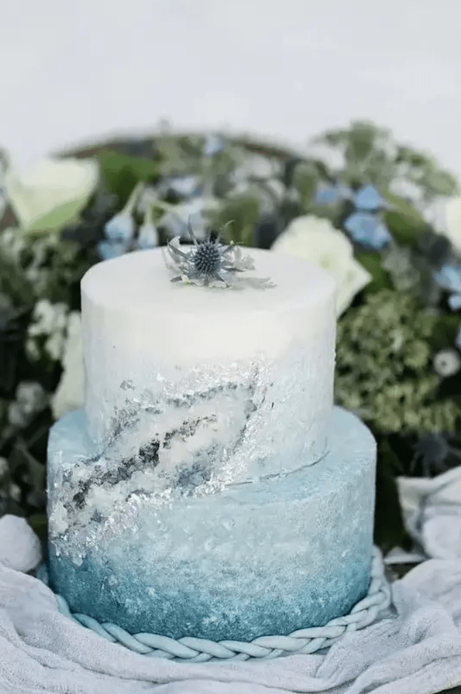 a beautiful ombre serenity blue winter wedding cake with crystals and a thistle on top the cake is lovely
