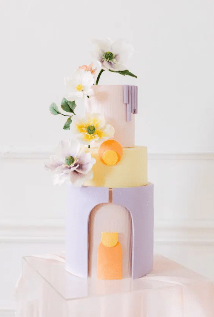 a beautiful pastel spring wedding cake with a blush, yellow and lilac tier, architectural details and blooms is wow