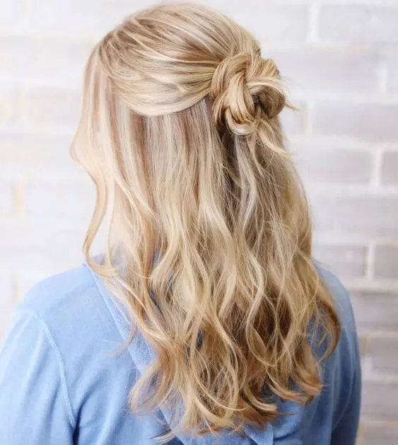 A catchy boho half updo with a messy wrapped knot and waves down plus face framing locks is cool
