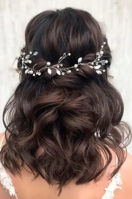 a charming twisted and wavy half updo with a volume on top accented with a pearl and rhinestone hair vine is a lovely idea