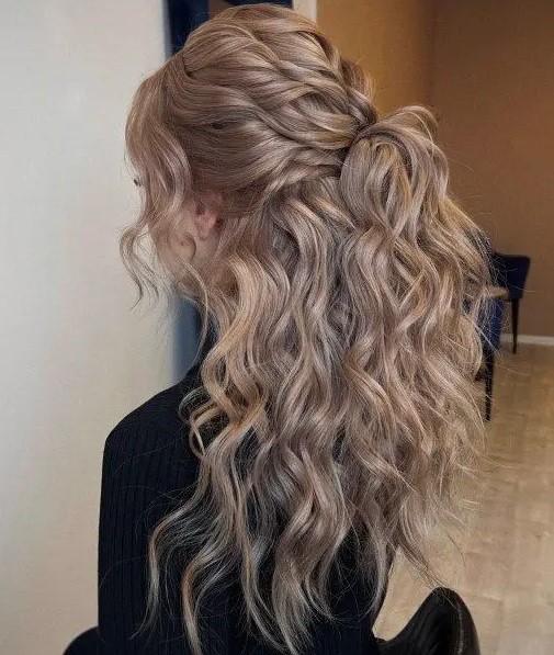 A cool half updo with a large twisted bump on top and waves down plus face framing locks for long hair