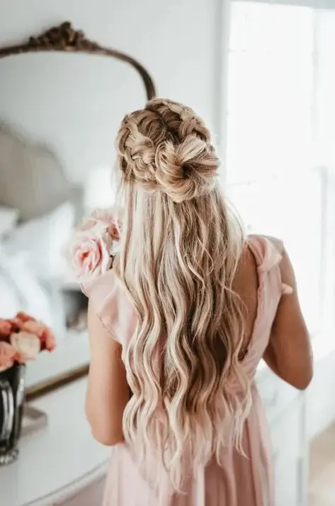 A dreamy half updo with two large braids on top and a top knot plus waves down for a fary tale look