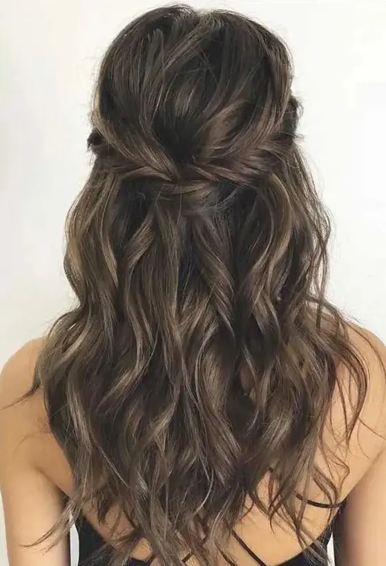 a long half updo with a braided halo and waves down is a chic and cool idea for a boho wedding