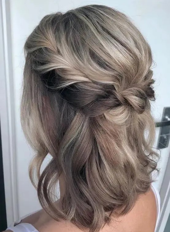 a medium half updo with blonde balayage, a braided halo and a bump and waves down is a timeless solution