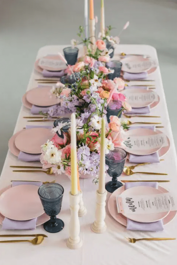 a modern pastel wedding tablescape with pink plates and lilac napkins, navy glasses, pastel candles and lovely florals