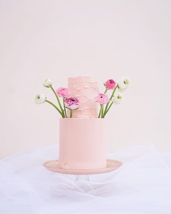 a pastel pink wedding cake topped with pink and white ranunculus is a unique idea for sprig