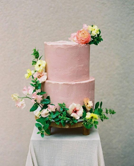 a pastel pink wedding cake with yellow, pink and coral blooms and greenery is amazing