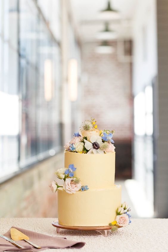 a pastel yellow wedding cake topped with pastel blooms is a lovely idea for a spring wedding