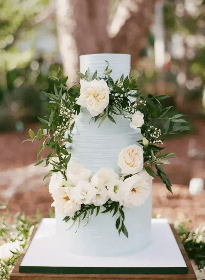 a serenity blue textural buttercream wedding cake decorated with white blooms and greenery for a spring or summer wedding