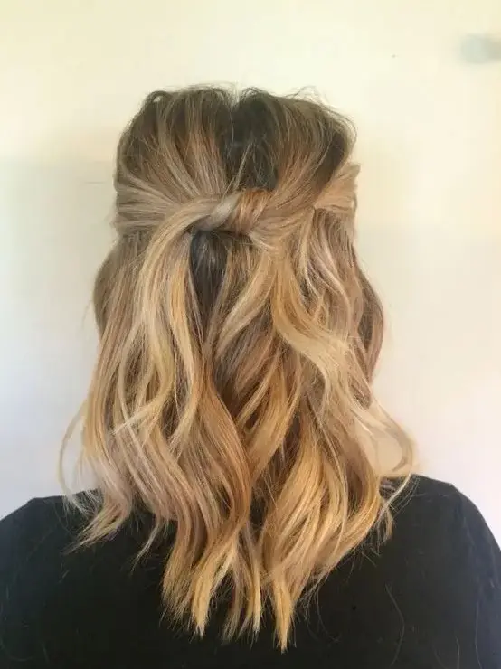 a simple and casual wavy half updo with a bump on top and a knot plus waves down is a stylish idea to rock