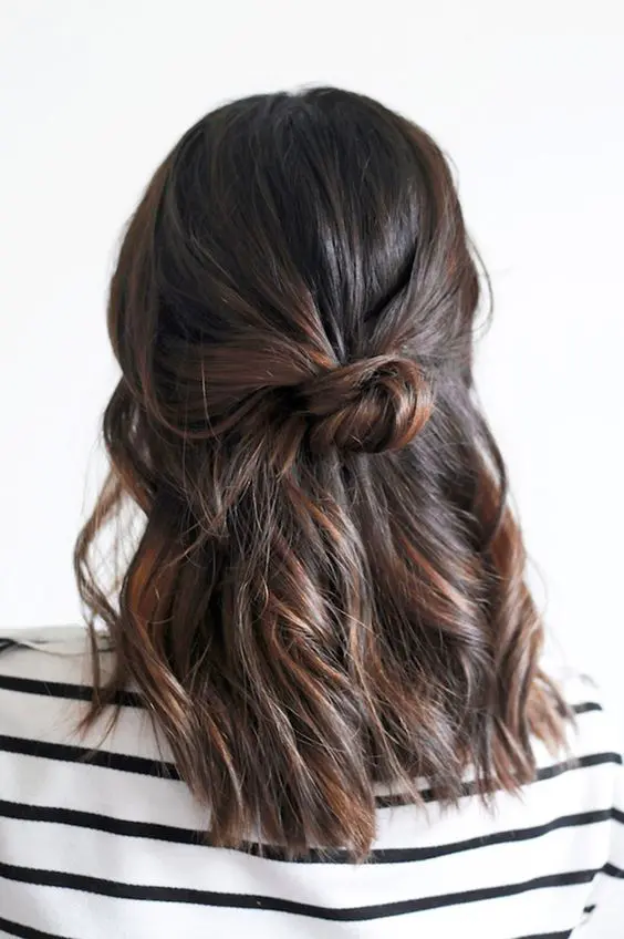 a simple half updo with a textured top, waves down and a bun is a cool idea for a bridesmaid