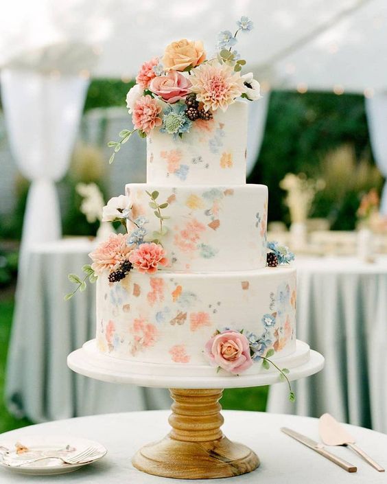 a white wedding cake decorated with pastel blooms painted on it and some fresh flowers all over