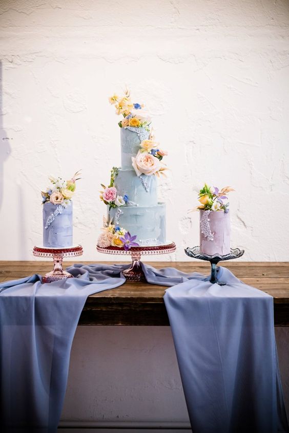 an arrangement of pastel wedding cake in lilac, mint blue and blue colors and topped with fresh blooms