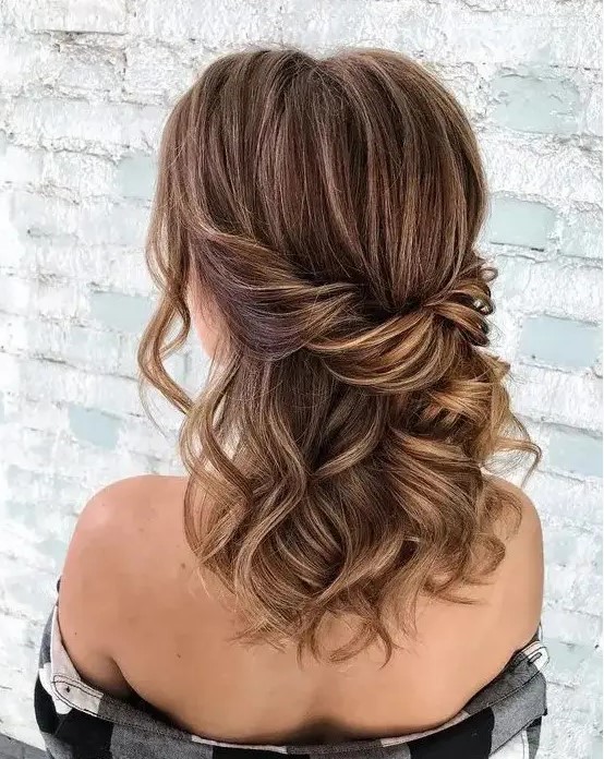An elegant brown half updo with caramel balayage and a twisted touch plus some waves down and face framing locks