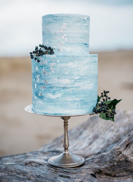 a blue watercolor wedding cake decorated with silver leaf and some berries for a coastal wedding