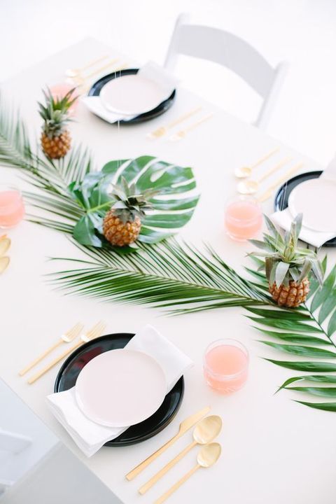 a stylish modern setting with tropical leaves, black plates, pineapples and gold flatware