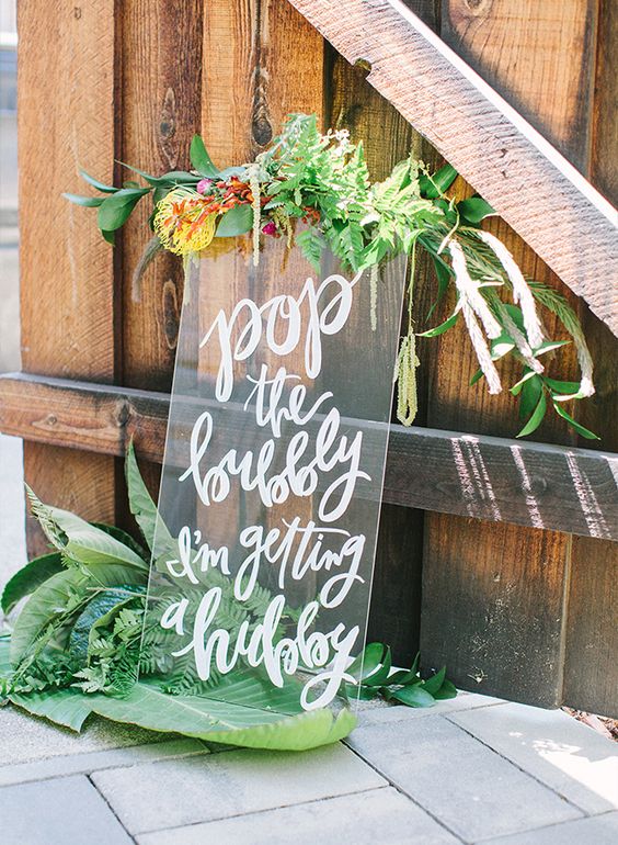 a sheer acrylic calligraphy sign decorated with greenery and blooms for the shower
