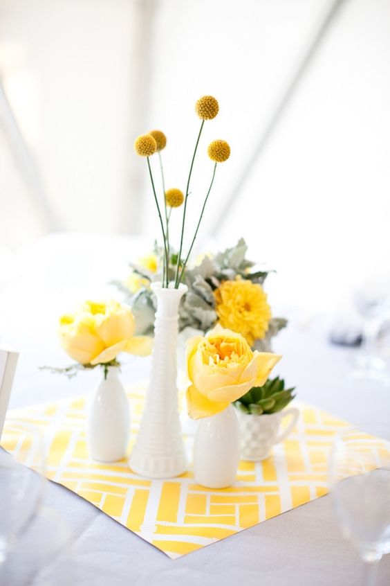 a wedding centerpiece with a printed napkin, yellow blooms and pale miller in white vases