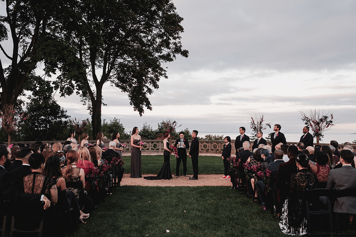 The wedding ceremony took place in the garden of the castle, the black chairs were decorated with deep red blooms
