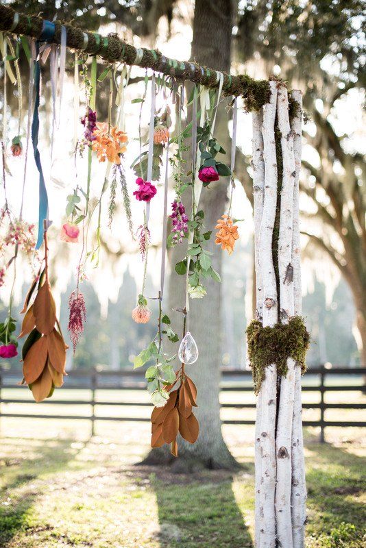 a boho wedding arch decorated with greenery and blooms hanging down from it