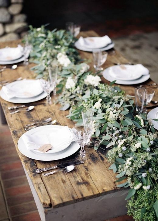 a very lush greenery table runner with berries and white blooms over a naked table