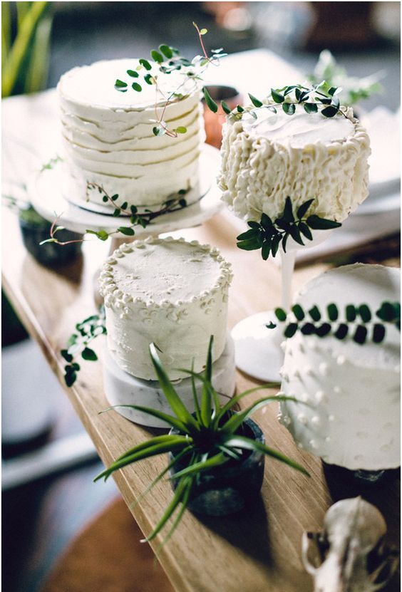 an assortment of white textural wedding cakes with fresh greenery on top