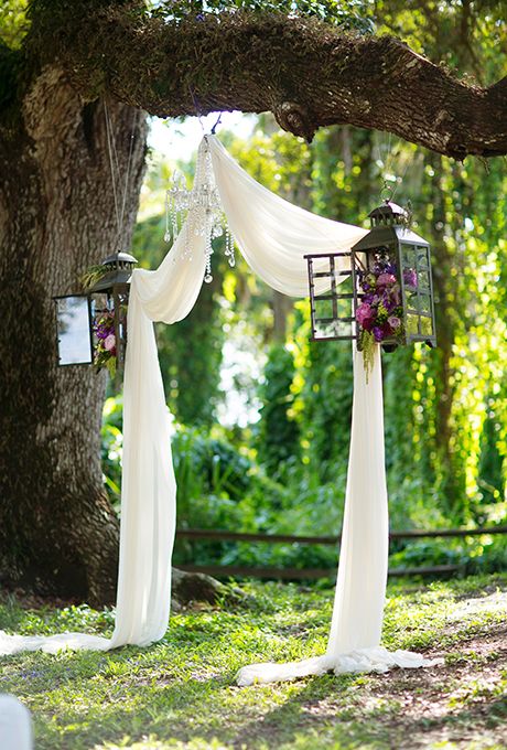 ethereal fabric hung as an arch, lanterns with flowers and a glam crystal chandelier for a wedding ceremony