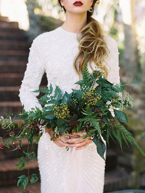 a heavily embellished high neckline long sleeve wedding dress and a lush textural greenery bouquet with berries
