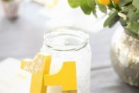 14 bold yellow table numbers decorated with white and grey lace and a mercury glass vase with yellow blooms