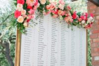 17 a framed seating chart topped with a lush and colorful floral garland