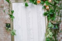 18 a framed seating chart with a very lush greenery garland and large blush blooms