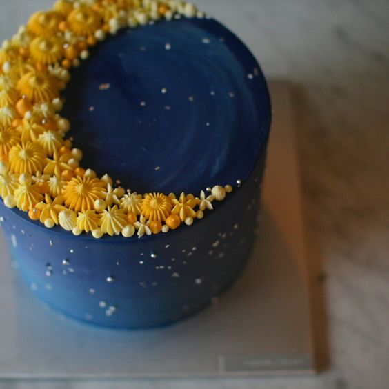 a blue wedding cake topped with a yellow crescent moon made of candies and meringues