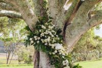 22 a large tree decorated with lush greenery and white blooms for a ceremony backdrop