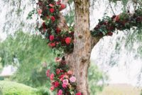 23 a tree covered with bold red, burgundy and pink blooms and greenery for a ceremony