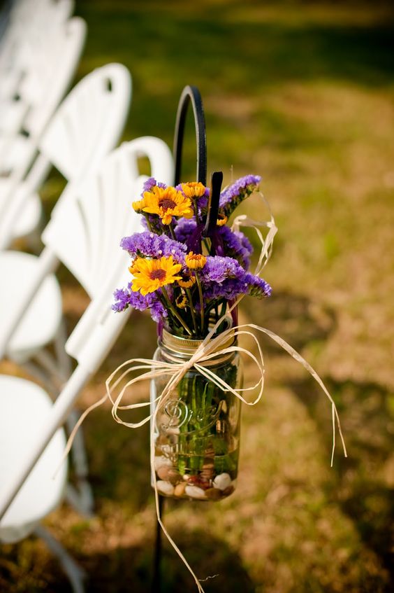 a mason jar with purple and yellow blooms plus twine for wedding aisle decor
