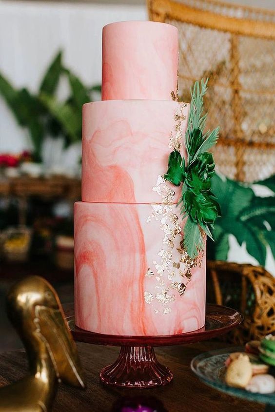 a pink marbleized wedding cake decorated with tropical leaves and gold leaf for a tropical wedding